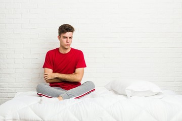 Young teenager student man on the bed frowning face in displeasure, keeps arms folded.