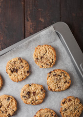 Homemade organic oatmeal cookies with raisins in baking tray on wooden background. Top view