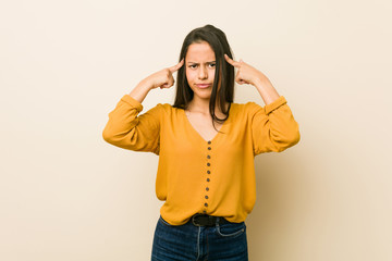 Young hispanic woman against a beige background focused on a task, keeping forefingers pointing head.