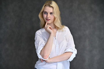 Portrait of a cute blonde girl, a young woman in a white shirt with beautiful curly hair on a gray background. Shows hands to the sides. Beauty, brightness, emotions.