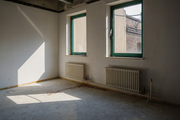 Interior view of empty abandon room with radiator heaters, glass windows and air duct system on ceiling.