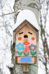 Smiley birdhouse. Birdhouse in the form of a funny face on the tree. Handmade wooden nesting box covered in snow. Winter landscape with trees covered of the snow and copy space.