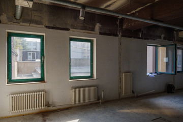 Interior view of empty abandon room with radiator heaters, glass windows and air duct system on ceiling.