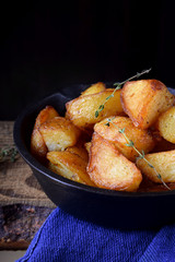 Golden roasted potato wedges in a cast iron pan against black background 