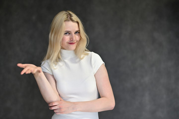 Portrait of a cute blonde girl, a young woman in a white sweater with beautiful curly hair on a gray background. Shows hands to the sides. Beauty, brightness, emotions.