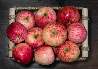 A basket of apples on a dark brown wooden background. Flat lay. Juicy ripe red fruit apples in the basket. Top view. Autumn harvest