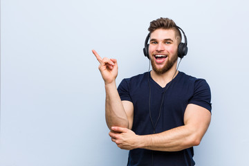 Young caucasian man listening to music smiling cheerfully pointing with forefinger away.