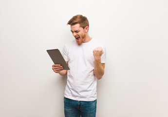 Young redhead man surprised and shocked. Holding a tablet.