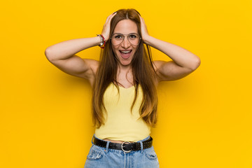 Young redhead ginger woman with freckless laughs joyfully keeping hands on head. Happiness concept.