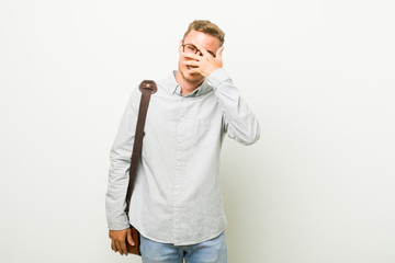 Young caucasian business man blink at the camera through fingers, embarrassed covering face.