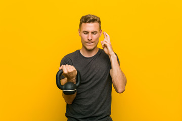 Young caucasian man holding a dumbbell crossing fingers for having luck