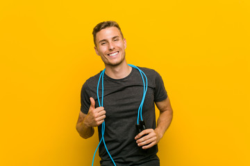 Young caucasian man holding a jump rope smiling and raising thumb up