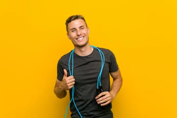 Foto op Canvas Young caucasian man holding a jump rope smiling and raising thumb up © Asier