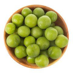 heap green cherry-plum in wooden cup isolated on white background. top view