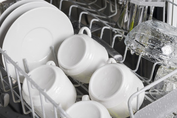 four clean white cups for coffee and saucers in the lattice of the dishwasher, closeup view