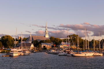 Fototapeta na wymiar Saint-Michel-de-Bellechasse marina seen during a late afternoon summer golden hour, with sailboats, historical 1873 church and waterside restaurant in the background, Quebec, Canada