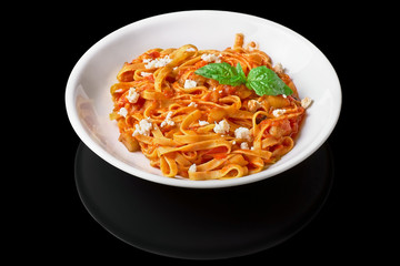 Heaped plate of delicious Italian spaghetti pasta with fresh basil leaves and cheese, on a black background Isolated
