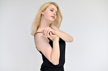 Portrait of a cute blonde student girl, a young woman in a black dress with beautiful curly hair on a white background in different poses. Shows hands to the sides. Beauty, brightness, emotions.