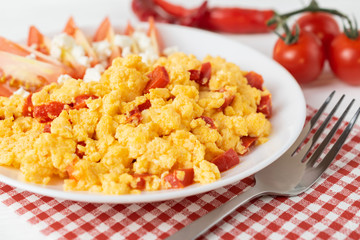 Close up scrambled eggs with pepper, tomatoes and cheese on a white plate