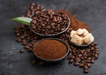 Fresh raw organic coffee beans with ground powder and cane sugar cubes with coffee trea leaf on black background.