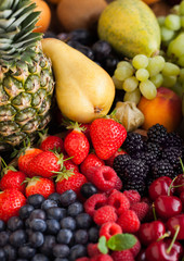 Fresh organic summer berries mix in wooden tray and exotic fruits on wooden background. Raspberries, strawberries, blueberries, blackberries and cherries. Watermelon, pear, pineapple, grapes, banana.