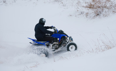 A motorcyclist on an ATV rides off-road in a snowy winter forest