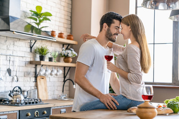 Beautiful young couple hugging while cooking dinner and drinking wine in the kitchen at home