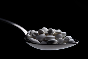 metal spoon with a bunch of pills on a black background