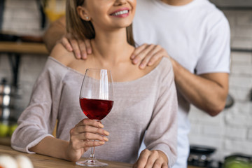 Cropped shot of beautiful girl drinking wine while handsome man making massage to her in home kitchen