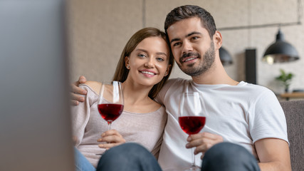 Couple drinking a glass of red wine in their living room while watching movie