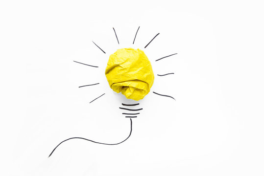 Business ideas. Composition of modern crumpled yellow paper ball and drawing of lamp bulb on white background. Creative and startup concepts.