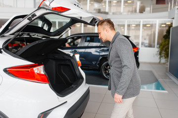 Man looks at the trunk of new car in showroom