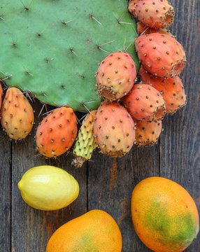 Exotic fruits on old wooden background. Opuntia cactus with large flat pads and red thorny edible fruits. Prickly pears fruit. Sabra Fruit. Sabra cacti, Mango and lemons on old wooden background 