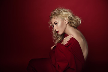 Beautiful portrait seductive woman with light blond hair,blue eyes and red lips posing in red coat and on dark red background. Fashion, glamour, concept