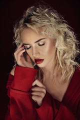 Beautiful portrait seductive woman with light blond hair,blue eyes and red lips posing in red coat and on dark red background. Fashion, glamour, concept