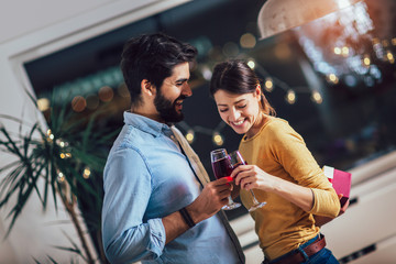 Beautiful young couple is celebrating at home. Pretty girl is giving her boyfriend a gift box
