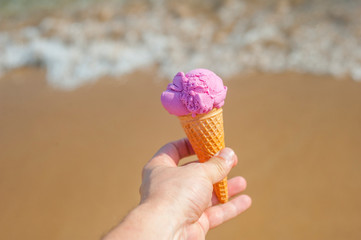 one hand holds tasty ice cream on a summer beach.