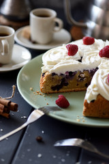 Homemade blueberry cake with coconut cream roses and raspberries served with coffee on dark background. Still life with natural lighting