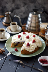 Fruit cake with coconut cream roses and raspberries served with black coffee on darkvbackground copy space. Still life with natural lighting
