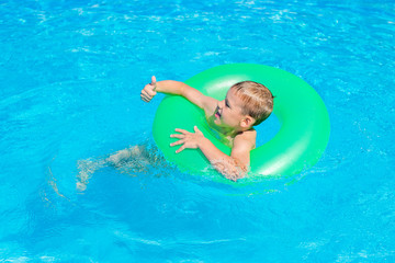 Happy kid boy having fun in an swimming pool. Active happy healthy preschool child learning to swim. With safe floaties or swimmies.