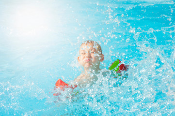 Happy kid boy having fun in an swimming pool. Active happy healthy preschool child learning to swim. With safe floaties or swimmies.