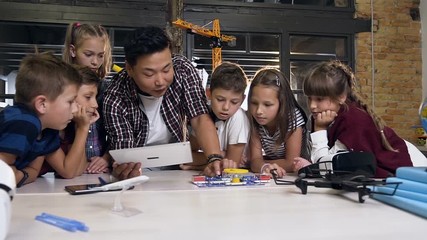 Shooting of group of six caucasian school children watching their Asian male teacher using the tablet launches an electrical constructor in class - Powered by Adobe