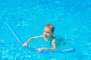 Fototapeta na wymiar Happy kid boy having fun in an swimming pool. Active happy healthy preschool child learning to swim. With safe floaties or swimmies.