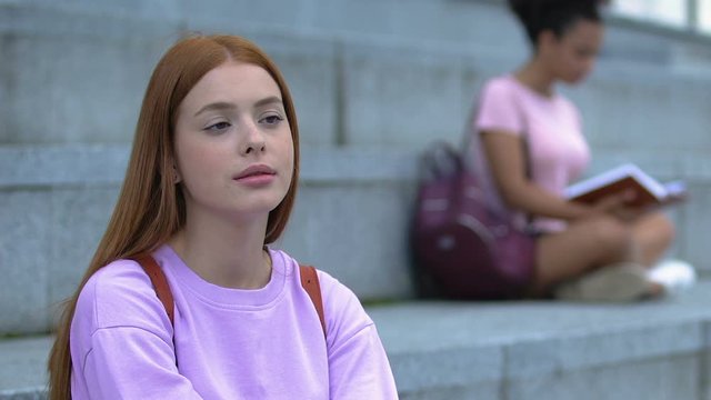 Thoughtful redhead teen female with rucksack sitting on academy stairs, student
