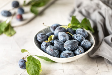 Dark blue plum in a plate on a white table.