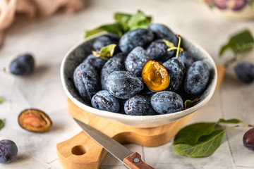 Dark blue plum in a plate on a white table.