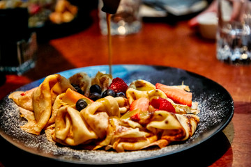 Pancakes with berries (blueberries and strawberries) are poured with caramel sauce.