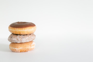 Three donuts stacked on one another, chocolate iced, blueberry cake, and plain glaze, white background, copy space