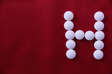 White round medical pills lie on a red background in the form of a letter H