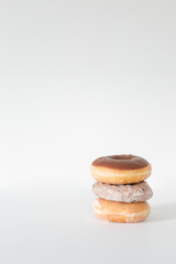Three donuts stacked on one another, chocolate iced, blueberry cake, and plain glaze, white background, copy space